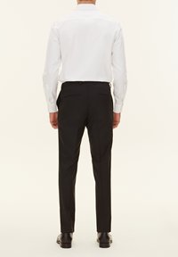 Camicia bianca a maniche lunghe con colletto classico, abbinata a pantaloni eleganti neri, caratterizzati da una texture liscia e infilata in vita.