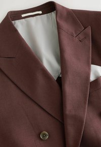 Blazer burdeos con una textura suave, solapa pico, cierre de un botón y un forro interior de un gris claro contrastante.