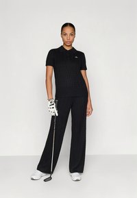 Črno pletena golf obleka, ki vključuje polo majico s kratkimi rokavi in široke hlače. Dodatki vključujejo golf palico in rokavico.