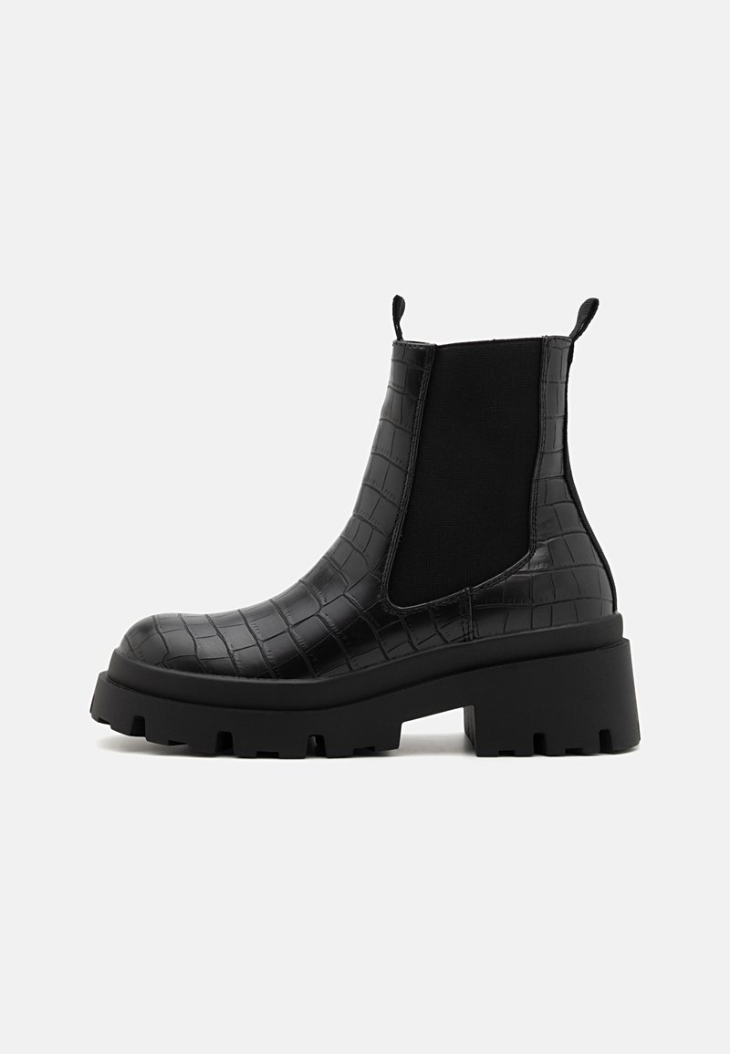 Bottine à semelle épaisse noire avec tige en cuir embossé croco et panneaux latéraux élastiques pour un enfilage facile.