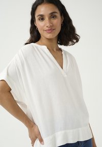 White linen blouse with a V-neckline, short sleeves, and relaxed fit. It features a subtle texture and a straight hemline.