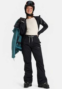 Snøsportantrekk med svart jakke og bukser, grå snor, lys baselayer og hjelm med fargerik visir. Sorte støvler.