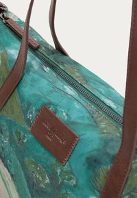 Sac à bandoulière avec imprimé nature bleu sarcelle et vert, anses en cuir marron, écusson logo en cuir marron et fermeture éclair noire.