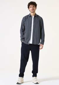 Camisa de botones con estampado náutico sobre una camiseta blanca, combinada con pantalones azul marino y zapatillas deportivas claras. Presenta un corte relajado y mangas cortas.