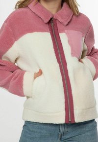 Polarowy rozpinany sweter w kolorze różowym i kremowym, z blokami kolorów, kieszenią z przodu i ściągaczami przy rękawach. Miękka tekstura i luźny krój.