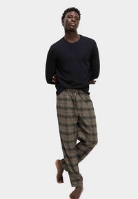 Dunkelnavyblaues Langarmshirt kombiniert mit locker sitzenden braunen karierten Hosen. Die Hosen haben einen elastischen Bund und eine weiche Textur.