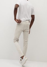 Vaqueros ajustados color beige claro con detalles de costura sutiles, combinados con una camiseta blanca lisa y zapatillas blancas con un acento en color marrón claro.