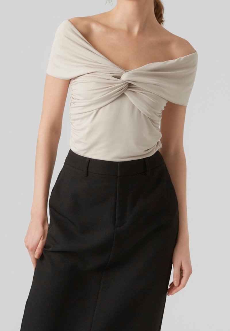 Top crema fuera del hombro con detalles fruncidos en la parte delantera, combinado con una falda negra de talle alto. Tejido suave y diseño ajustado.