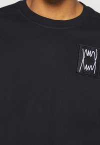 Granatowy sweatshirt wykonany z bawełny, z teksturowaną naszywką z białym przeszyciem. Okrągły dekolt i gładki, miękki materiał.