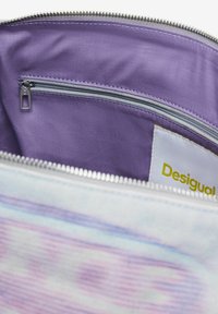 Die Innenseite des Desigual-Pouches verfügt über ein lila Stofffutter und eine Reißverschlusstasche mit einem silbernen Reißverschluss. Der Hauptstoff hat ein pastellfarbenes Muster.