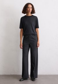 Schwarzes T-Shirt mit kurzen Ärmeln, kombiniert mit hoch taillierten, weit geschnittenen schwarzen Hosen. Glattes Material mit lockerer Passform und elastischem Bund.