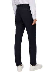 Marineblauwe broek van stof met een gladde textuur; heeft een slim fit, een achterzak met knoop en wordt gedragen met witte sneakers.