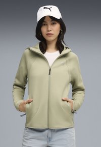 Felpa zip con cappuccio di colore verde chiaro, dotata di due tasche frontali, dettagli a coste e un logo riflettente sul lato sinistro del petto.