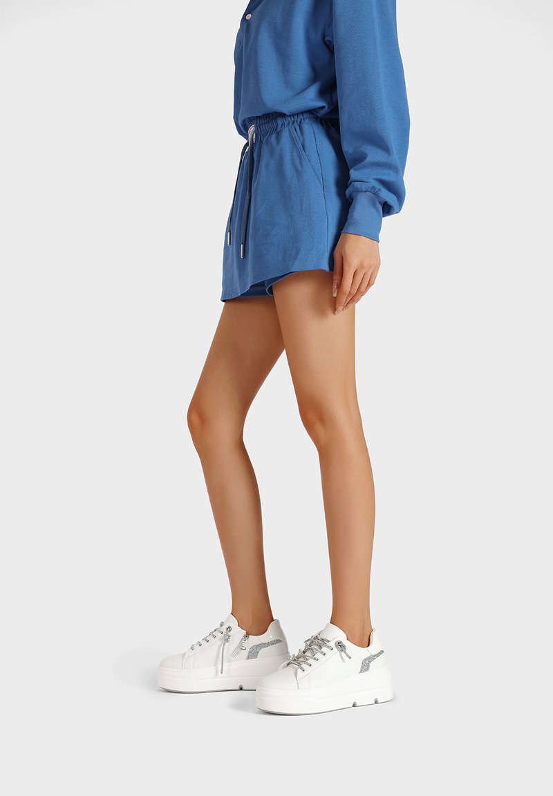 Felpa blu con maniche lunghe, abbinata a pantaloni corti coordinati. Le scarpe sono delle sneaker con suola platform bianca, dettagli in argento e lacci.