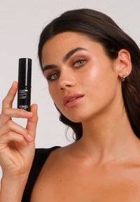 Schwarzer zylindrischer Kosmetikbehälter mit der Aufschrift "KIKO Sculpting Touch", gehalten von einem Model mit einem glatten Teint, das ein schwarzes Oberteil trägt.