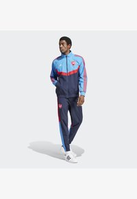 Herren-Trainingsanzug in Blau, Rot und Marine, mit Reißverschlussjacke mit Logo, gestreiften Ärmeln und passenden Hosen mit Logo und seitlichen Nähten.