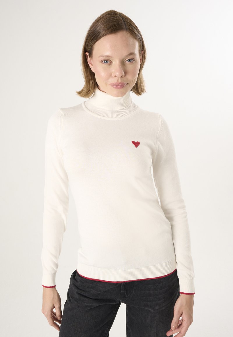Witte turtleneck trui met een geribbelde textuur, voorzien van een klein rood hartlogo op de borst en rode accenten op de manchetten en de onderrand.