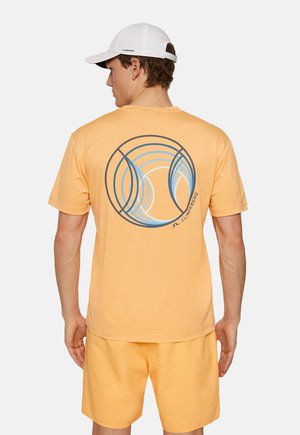 Oranje T-shirt met korte mouwen en cirkelvormige blauwe grafiek op de achterkant, gecombineerd met bijpassende oranje shorts. Witte pet gedragen op het hoofd.