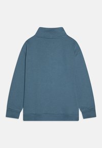Plavi pulover s mekim materijalom, visokim ovratnikom, dugim rukavima, rebrastim manžetama i rubom, jednostavnog dizajna, bez vidljivih logoa ili uzoraka.