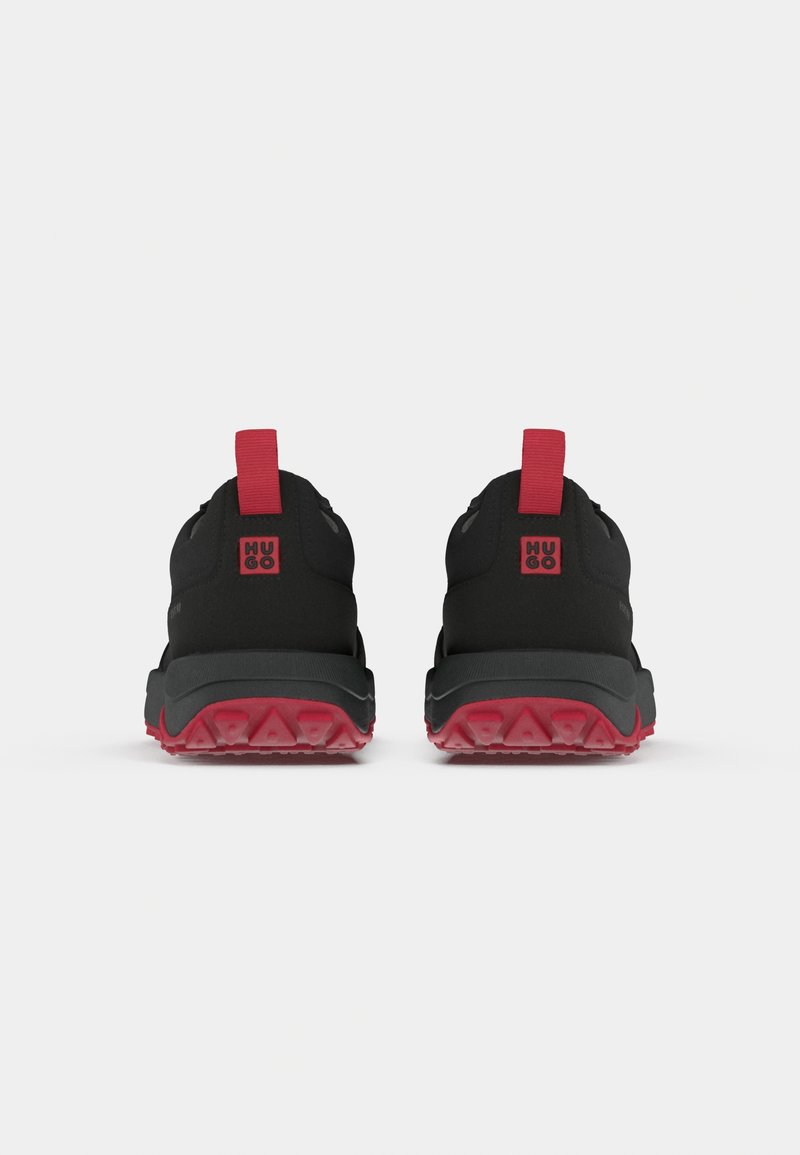 Schwarze Sportschuhe mit roten Akzenten, die ein robustes Design, eine strukturierte Gummisohle und Ziehlaschen für ein einfaches Anziehen aufweisen.