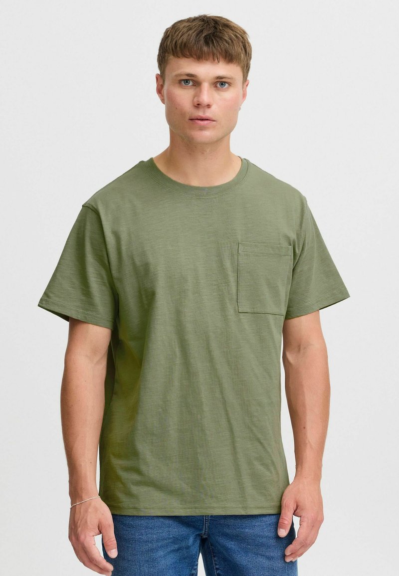 Camiseta de manga corta en verde oliva hecha de algodón texturizado. Presenta un cuello redondo y un bolsillo cuadrado en el lado izquierdo del pecho.