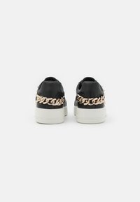 Sneaker in pelle nera con unaccento di catena d'oro chunky sul retro, suola in gomma bianca e superficie liscia.