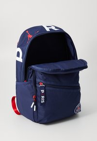 Navy backpack in durable material with red accents, large front pocket, zipper closure, and printed "PARIS" and logo details.