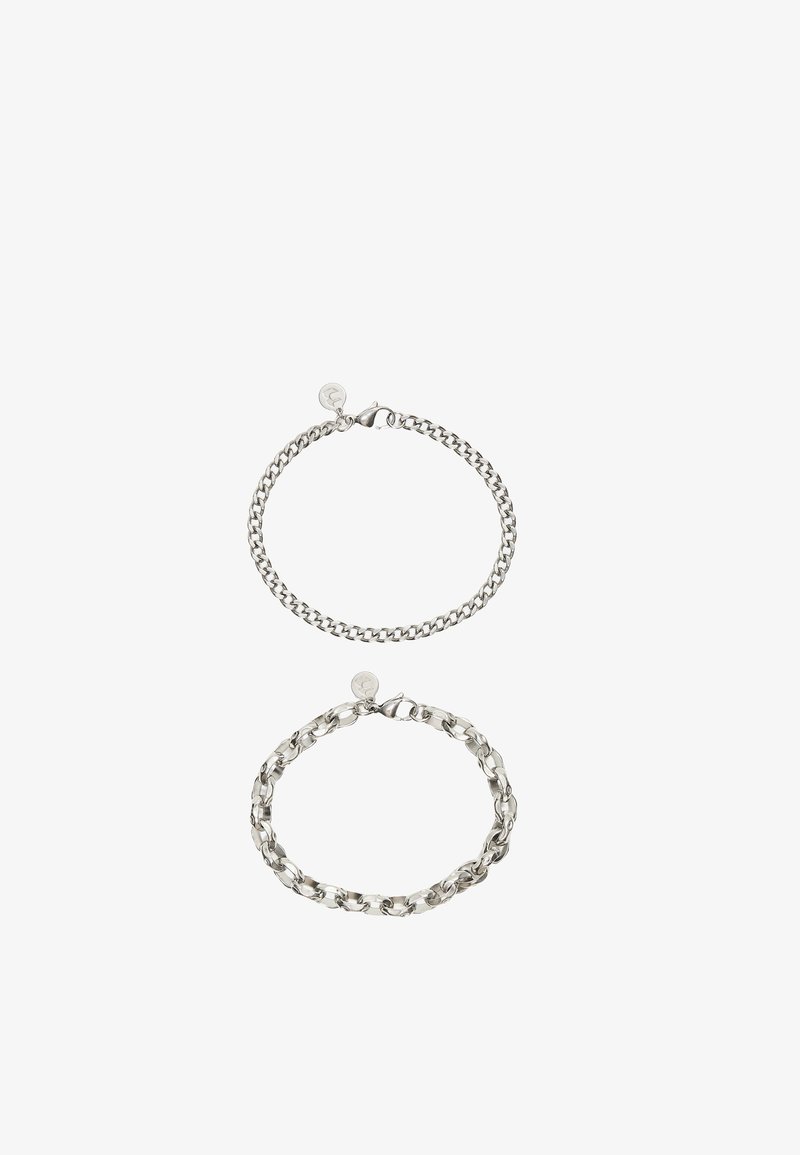 Deux bracelets chaîne en argent avec fermoirs mousquetons, l’un avec de petits maillons serrés et l’autre avec des maillons plus grands et ouverts, chacun avec une petite étiquette ronde.
