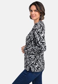 Langärmliges Oberteil in Schwarz und Weiß mit floralem Muster; aus weichem Stoff gefertigt; mit Rundhalsausschnitt und seitlichen Schlitzen am Saum.