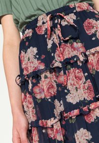 Sinih kukkur floral skirt dengan bunga merah muda dan putih, pinggang elastis dengan tali serut, dipadukan dengan kaos hijau bergaris.