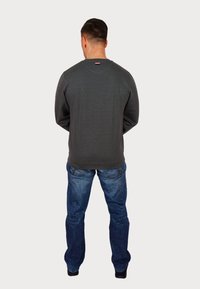 Jersey gris de manga larga, cuello redondo y pequeña etiqueta con logo en la parte trasera, combinado con vaqueros azules y zapatos negros.