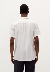 Camisa blanca de manga corta con sutiles rayas verticales, cuello abotonado y dobladillo recto. Tejido suave y corte relajado.
