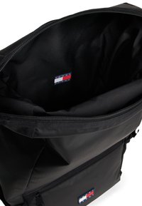 Musta reppu, jonka pinta on sileä; siinä on tilava sisäosa ja logotunniste pohjassa. Vetoketjukiinnitys ja vahvistetut ompelusaumat.
