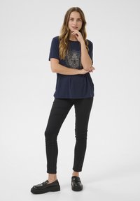 T-shirt bleu marine avec un graphique doré décoratif d'un lion, à manches courtes et coupe décontractée, associé à un jean skinny noir et des chaussures noires.