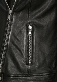 Svart läderjacka med en närbild av en dragkedjeficka. Har silverfärgade detaljer och en slät, texturerad yta.