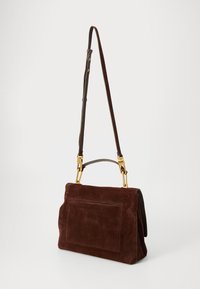 Sac à main en suède marron avec une forme structurée, comportant une poche avant, des accessoires en métal doré et une bandoulière amovible.