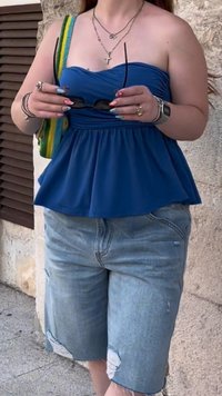 Mėlyna peplum palaidinė su prigludusia kūno dalimi ir platėjančiu apvadu, derinama su šviesiai mėlynomis dėvėtomis džinsinėmis šortais. Aksesuarai apima saulės akinius ir sluoksniuotas kaklo grandines.