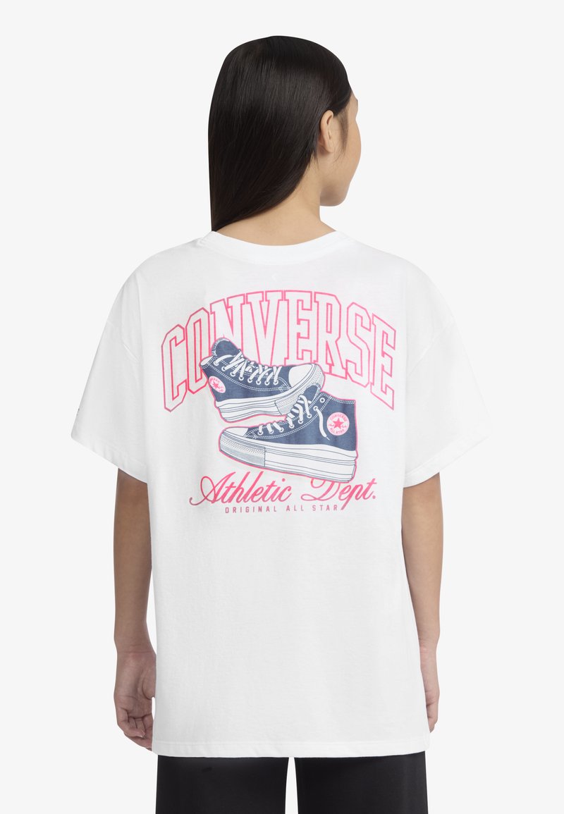 Balta per didelį T-shirts su mėlynomis sportinėmis batelėmis, ant nugaros ryškiai raudonas užrašas "CONVERSE" ir "Sporto skyrius".