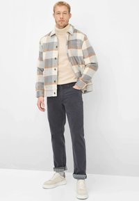 Kariertes Flanellhemd in Grau, Creme und Rost, kombiniert mit einem beigefarbenen Rollkragenpullover, dunkler Hose und cremefarbenen Sneakern mit strukturierten Details.