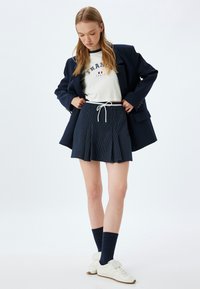 Navy plissé rok, gestreepte textuur, bijpassende koord taille. Witte grafische T-shirt met "Frankrijk" tekst, gelaagd onder een marineblauwe blazer en sokken.