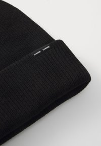 Black knit beanie made of soft material with a folded cuff, featuring a black label with white text that reads "SAMSØE."