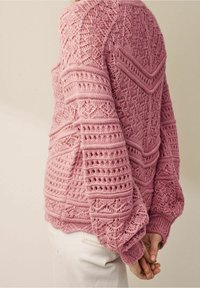 Różowy sweter z dzianiny z misternymi wzorami koronkowymi, fakturowanymi rękawami i detalem ściągacza na dole. Zaprojektowany z okrągłym dekoltem i luźnym krojem.