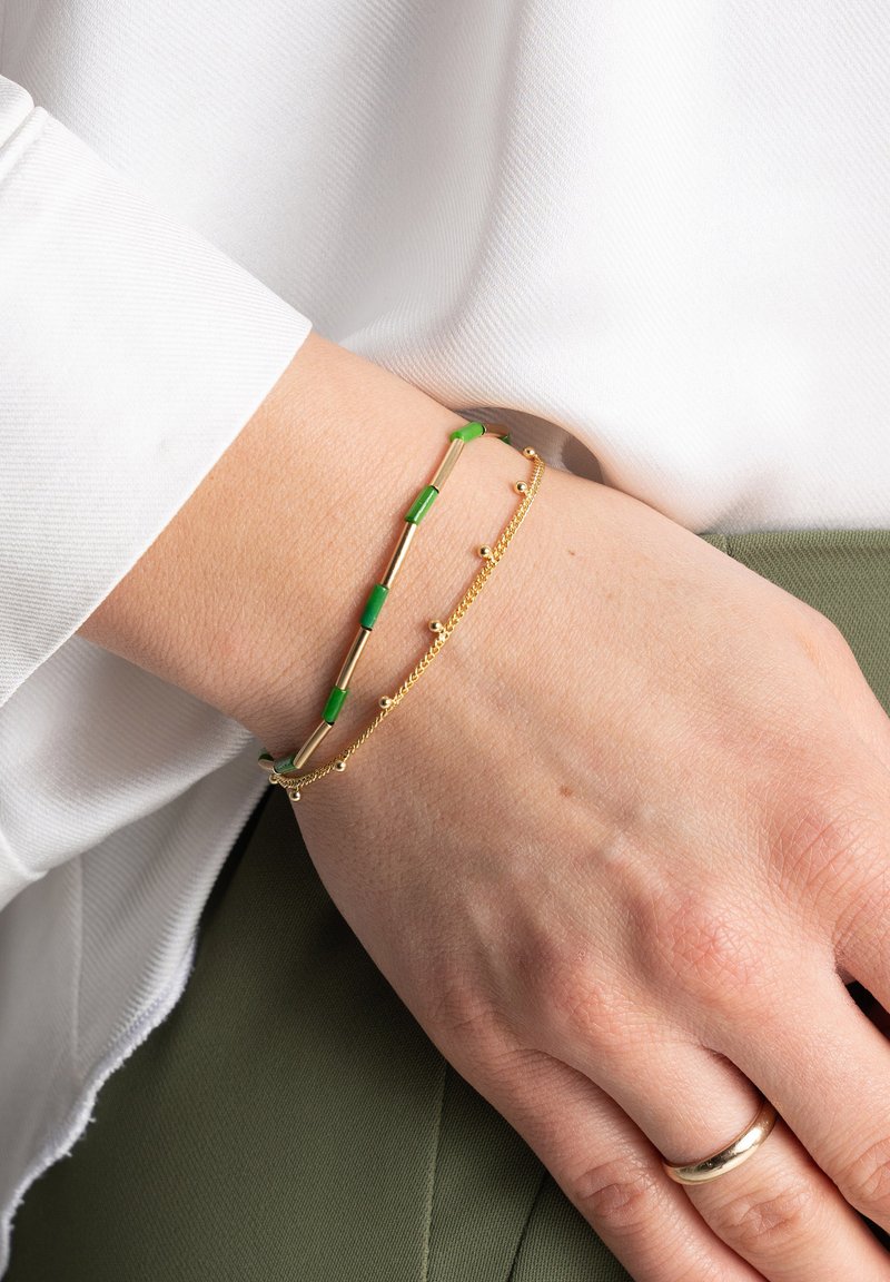 Złote bransoletki z zielonymi akcentami; jedna ma wydłużone sekcje, podczas gdy druga ma małe koralikami na łańcuszku.