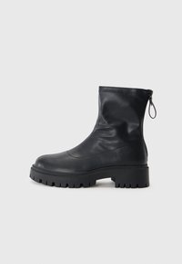 Zwarte enkelboot van soepel leer, met een ronde neus, dikke rubberen zool met een robuust profiel en een ritssluiting aan de achterkant.