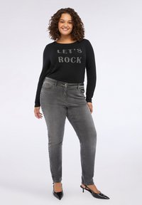 Top negru cu mânecă lungă și inscripția "LET'S ROCK" din strasuri, asortat cu blugi gri ce au studuri pe lateral. Modelul poartă pantofi cu toc negri.