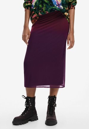 Personne portant une jupe mi-longue violette, un pull fleuri coloré et des bottes de combat noires à lacets, debout sur un fond blanc.