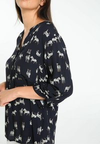 Blouse marine à motif zèbre blanc, avec des manches retroussables et une coupe décontractée. Tissu doux avec un léger éclat, devant boutonné.