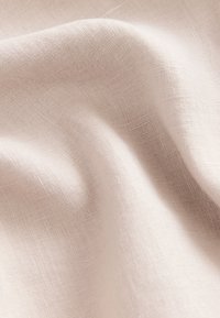 Light beige linen fabric with a soft, textured weave. The material drapes softly, featuring subtle variations of color throughout.