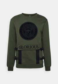 Donkergroene sweatshirt met zwart rond embleem featuring een bij en kroon, "Glorious Gangsta" tekst, zwarte banden, en "GLORIOUS" geborduurde voorpaneel.