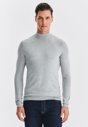 Jasnoszary, długi sweter z golfem o gładkim splocie, dopasowany fason, z prążkowanymi mankietami i spodem, zestawiony z ciemnymi dżinsami.